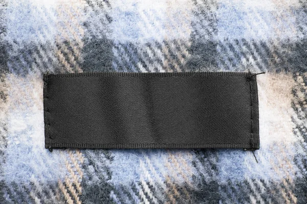 空白黑纺织品服装标签在羊毛格子背景背景 — 图库照片