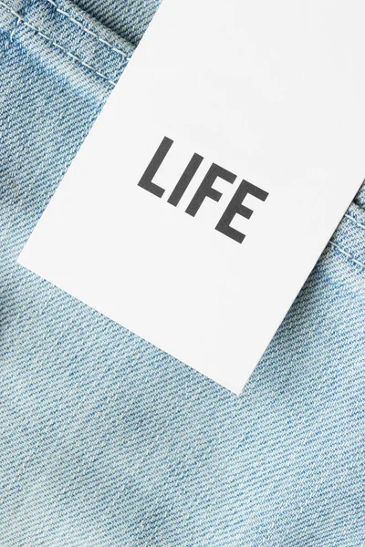 Clothing label says life on blue denim background closeup