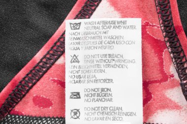 Pembe ve siyah tekstil arka planında farklı dillerde bakım giyim etiketi