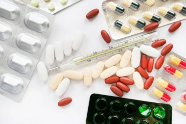 Bir sürü ilaç ve beyaz arka planda bir termometre.