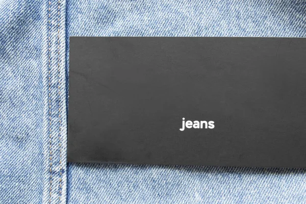 Black clothing label says jeans on blue denim background closeup