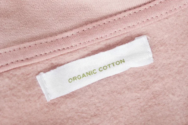 Clothing label says organic cotton on pink textile background