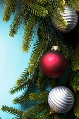Kırmızı ve gümüş topları mavi arka planda olan Noel ağacı dalı