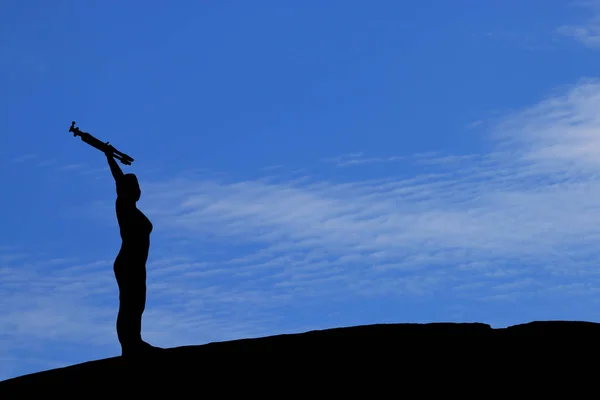 Silhouette einer Frau, die ein Stativ unter blauem Himmel hebt. — Stockfoto