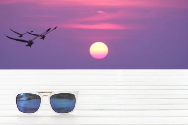 Sonnenbrille auf dem Tisch mit verschwommenen Vögeln, die zwischen Sonnenaufgang fliegen — Stockfoto