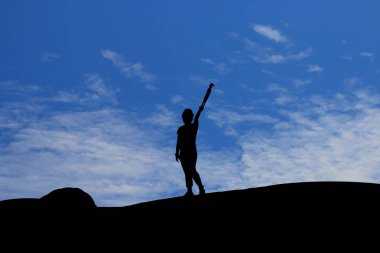 Mavi gökyüzünün altında tripod kaldıran kadının silueti.