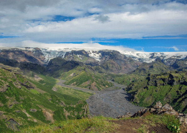 Stunning landscape of Myrdalsjokull glacier with green forest, bright white glacier and blue sunny sky, trekking trail in Thorsmork, Highlands of Iceland