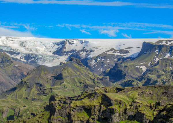 Breathtaking view on Myrdalsjokull glacier with green mountains, white ice and blue summer sky, hiking in Thorsmork, Highlands of Iceland