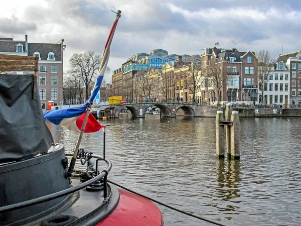 Holenderską banderę na łodzi z mostu i Amsterdam słynny holenderski flamandzki tradycyjne cegły budynki — Zdjęcie stockowe