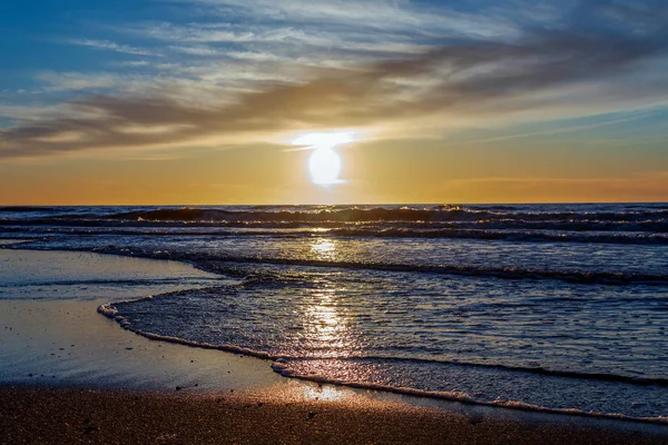 Homok strand végtelen horizonton, és habos hullámok alatt ragyogó naplementés sárga színek és felhők felett a tenger — Stock Fotó