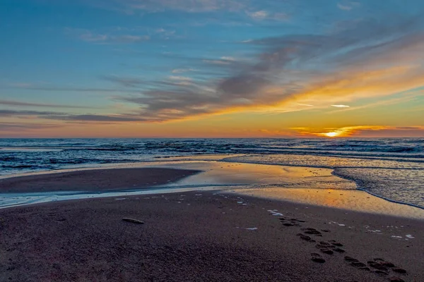 Homok strand végtelen horizonton, és habos hullámok alatt ragyogó naplementés sárga színek és felhők felett a tenger — Stock Fotó