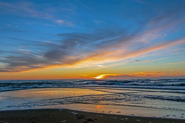 Plage de sable avec un horizon sans fin et des vagues mousseuses sous le coucher du soleil lumineux avec des couleurs jaunes et des nuages au-dessus de la mer — Photo