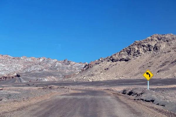 Desert road curve in Atacama: yellow sign and barren landscape of desert Stock Picture