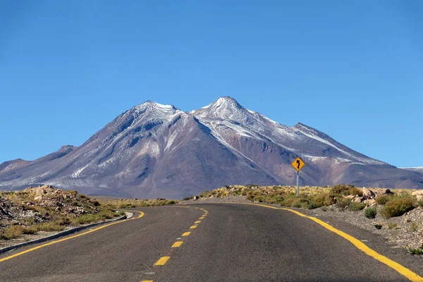 Wüstenstraßenkurve in atacama: Gelbes Schild und karge Wüstenlandschaft lizenzfreie Stockfotos