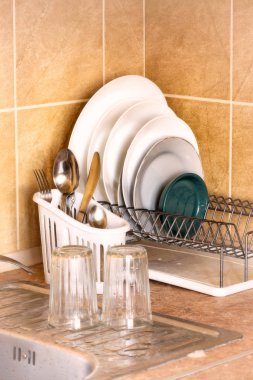 Washed plates, cutlery and glasses, drying in their racks close to the sink in the kitchen clipart