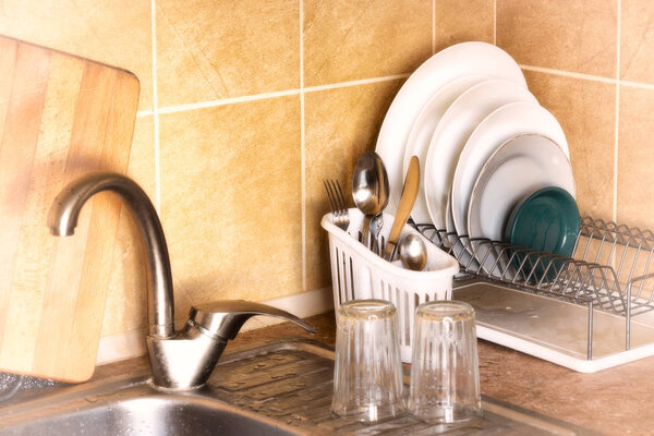 Washed plates, cutlery and glasses, drying in their racks close to the sink in the kitchen