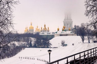 Kiev Pechersk Lavra manastırı altın kubbe ve çan kulesi disapearing arkasında bir soğuk kış günü Kiev, Ukrayna sırasında düşen kar manzarası. Sonsuz şöhret Park ön planda