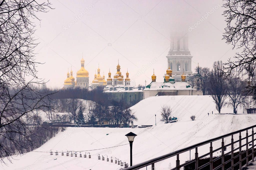 View of the Kiev Pechersk Lavra monastery golden domes and the bell tower disapearing behind the falling snow, during a cold winter day in Kiev, Ukraine. In foreground the Park of Eternal Glory