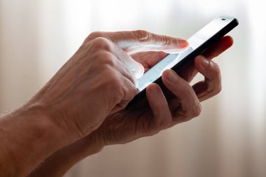 Adam sabah pencere kapalı perdeler ile yakın siyah bir smartphone'un dokunmatik ekranda parmağınızla yazmaya