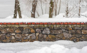 Kamenná stěna pokrytá čerstvý sníh v zimě. Sněhové vločky padají tiše. Stromy se objeví na pozadí