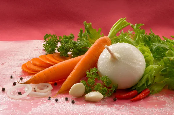 Vegetables - carrots with tops, red hot chili peppers, onions, black peppercorns, garlic, parsley and lettuce on a red background