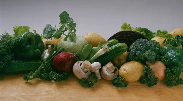 Vegetables - cucumber, onion, green onions, red onions, potatoes, red cabbage, broccoli, kohlrabi, mushrooms, bean pods, pepper, garlic, lettuce, curly parsley, dill on a light background and on a wooden table