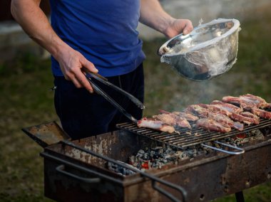    Metal maşa ile adam eli ızgara kuzu parçaları döner
