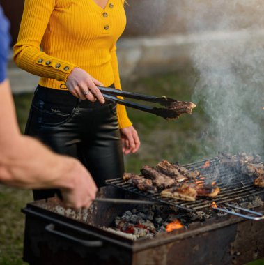 Metal maşalı bir kızın eli kuzu parçalarını ızgaraya çevirir.   
