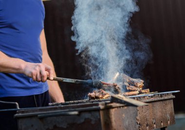    Metal maşa ile adamın eli gril üzerinde kuzu parçaları döner