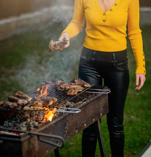 A mão de uma menina com pinças de metal transforma os pedaços de cordeiro em uma grade — Fotografia de Stock