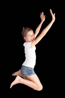 Genç kız için eğlenceli ve sevinç silah ile havada atlama gergin ve bacaklar bükülmüş siyah arka plan üzerine beyaz gömlek ve kot şort giyen izole. Meme veya hayatı kutlamanın poster için ilham kaynağı.