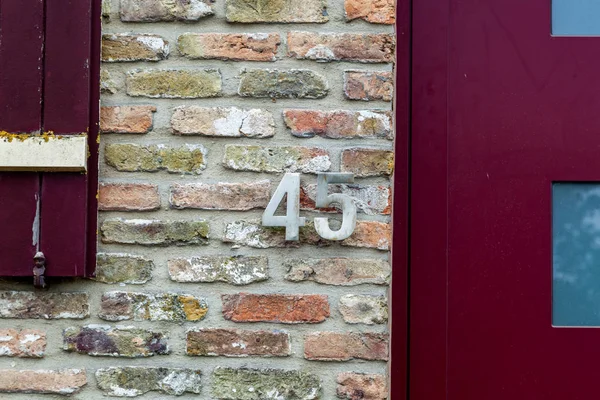 House number forty-five 45 made from silver metal in designer font weathered or tarnished on red yellow brick house wall in Belgium