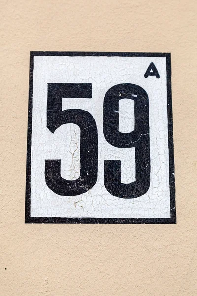 House number fifty-nine 59 in black on beige background on white painted rendered house wall in Belgium