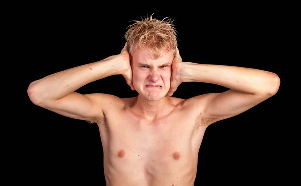 A young angry man unwilling to listen during an argument face screwed up, angry eyes, hands to ears, grimacing in landscape format on black background with copy space