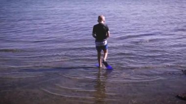 Genç bir çocuk yüzgeçleriyle sudan geriye doğru nasıl yürüyeceklerini gösteriyor. Yaz tatili kampı örneği için uygun video.