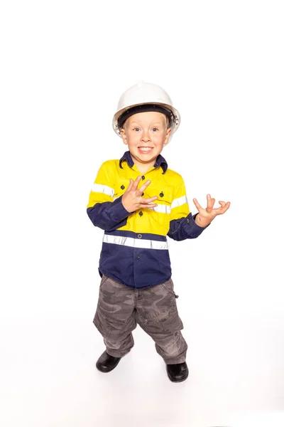 Junge blonde kaukasische Junge Hände ausgestreckt Rollenspiel als frustrierter Bauarbeiter Supervisor in einem gelb-blauen hallo-viz Hemd, Stiefel, weißen Hut, ohne Hammer und Maßband. Stockbild