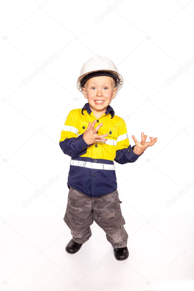 Young blond caucasian boy hands outstretched role playing as a frustrated construction worker supervisor in a yellow and blue hi-viz shirt, boots, white hard hat, without a hammer and tape measure.