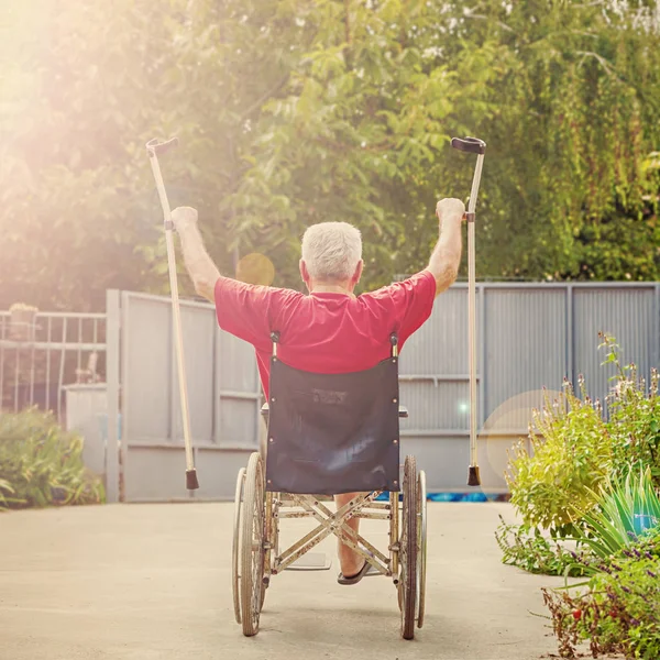 Back View of an older, handicapped man, arms and crutches raised in happiness, sunflare