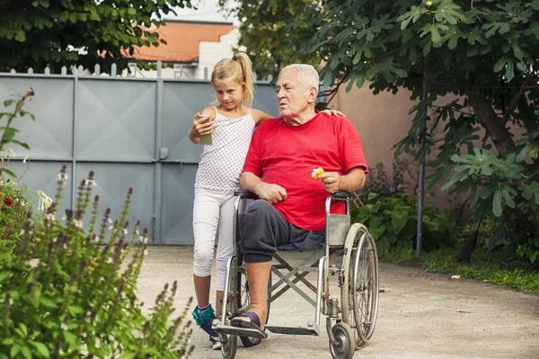 8 year old happy granddaughter helping her disabled grandfather outside making selfie