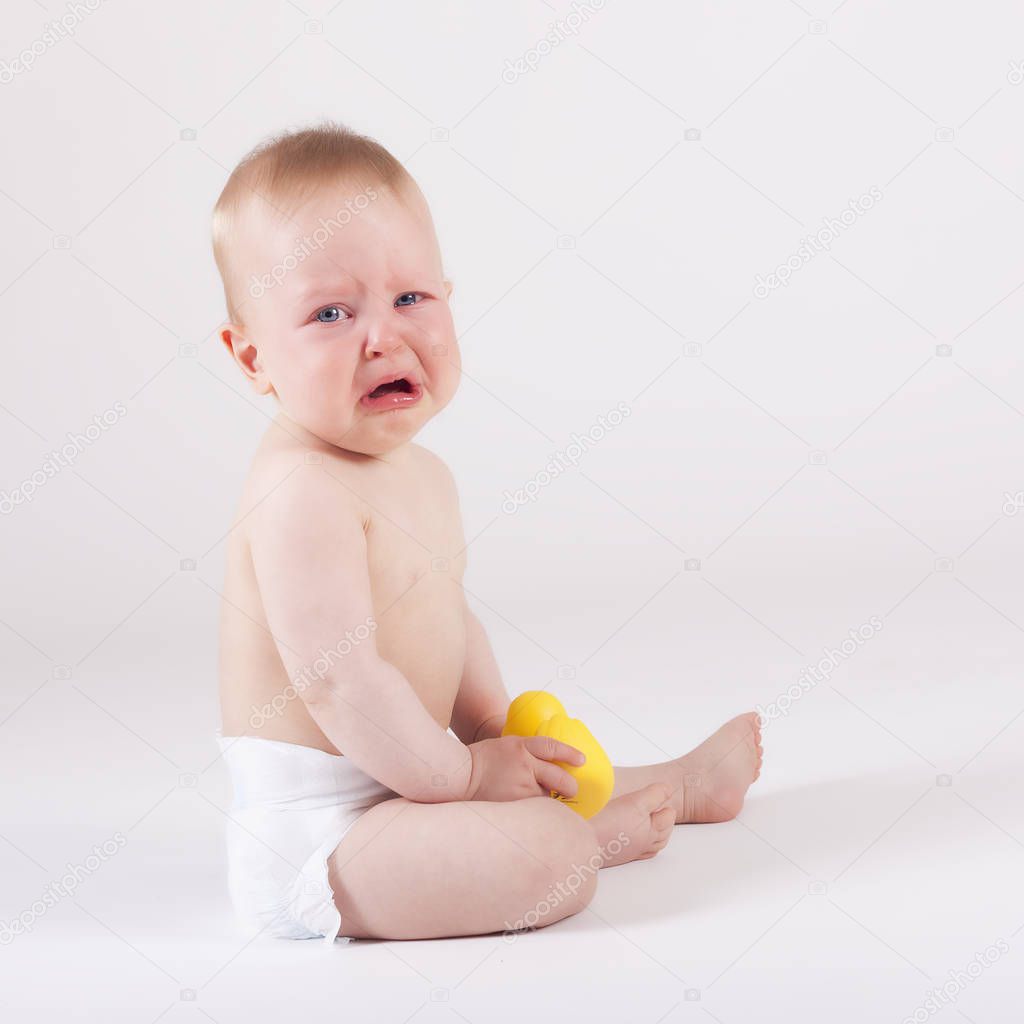Beautiful nine month crying baby in diaper sitting on the ground - studo shoot