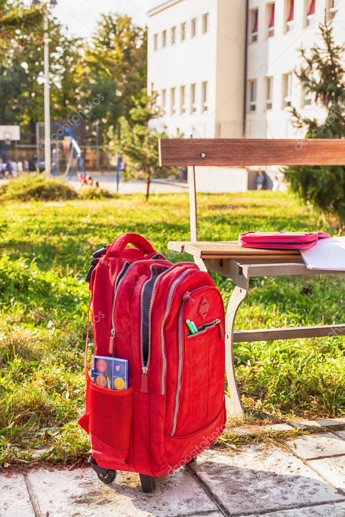 Modern red weightless school bag by the bench on the schoolyard