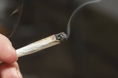 Yanan esrar koyu gri arka plan karşı ortak tutan bir el yakın çekim görüntüsü