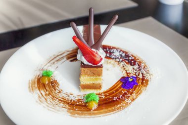 Karamel ve çilek, beyaz yuvarlak tabakta ile Fındıklı çikolatalı pasta dilimi bir Pastane çiçeklerle dekore edilmiş