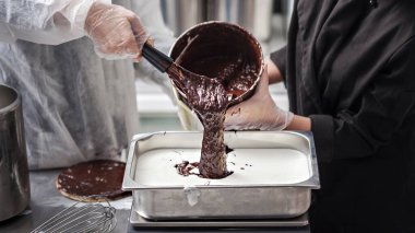 Kadınlar eldiven giyip çikolatalı dondurma hazırlıyorlar. Paslanmaz çelik tepsiye çikolata ganache döküyorlar.