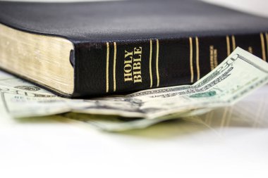 Beyaz arka planda yirmilik banknotla izole edilmiş kutsal bir Hristiyan İncili..