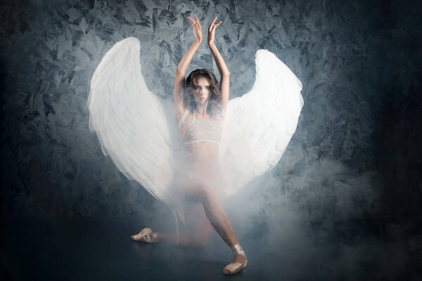 Ballerina in lace lingerie and angel wings dancing on dark stone background