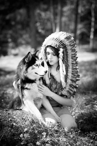 Young woman in traditional red indian warbonnets posing with black husky, monochrome
