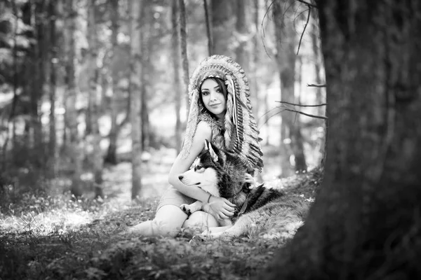 Young woman in traditional red indian warbonnets posing with black husky, monochrome