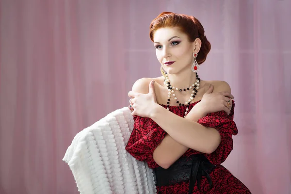 ヴィンテージの髪型とヴィンテージの椅子に座っている赤いドレスのメイクアップの豪華な若い女性 — ストック写真