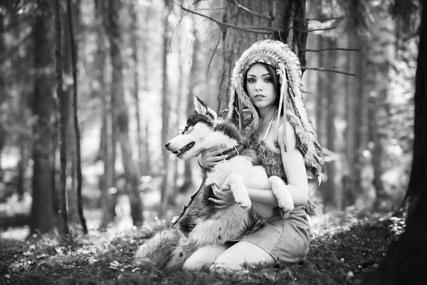 Young woman in traditional red indian warbonnets posing with black husky, monochrome